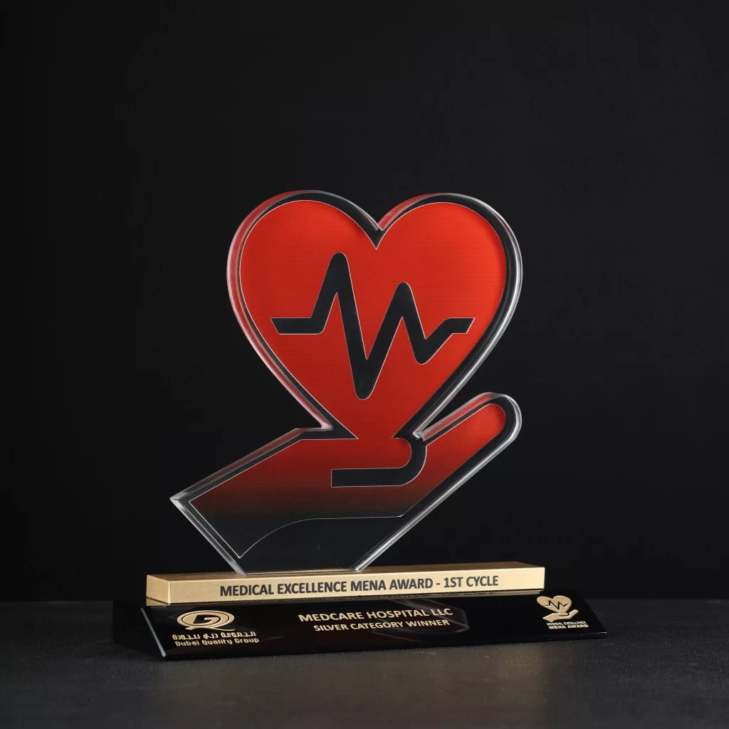 Custom heart symbol in hand-shaped crystal award with red and golden finish on a black base, created for the Medical Excellence MENA Award by Dubai Quality Group.