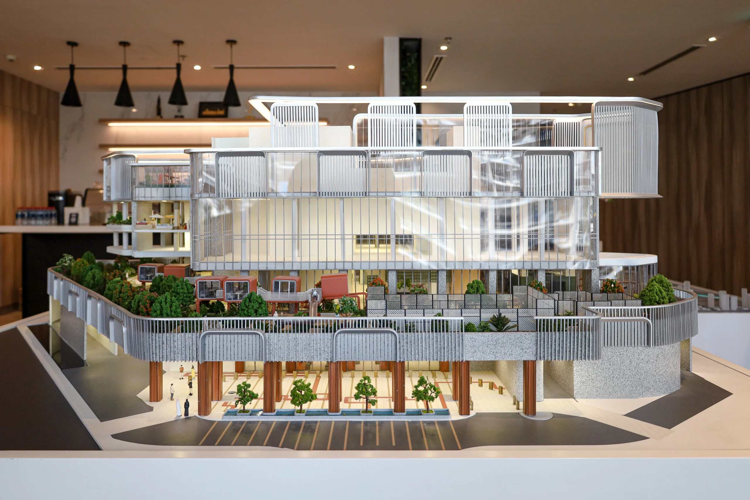 Detailed architectural scale model of a modern mixed-use development with terraces, landscaping and illuminated interiors.